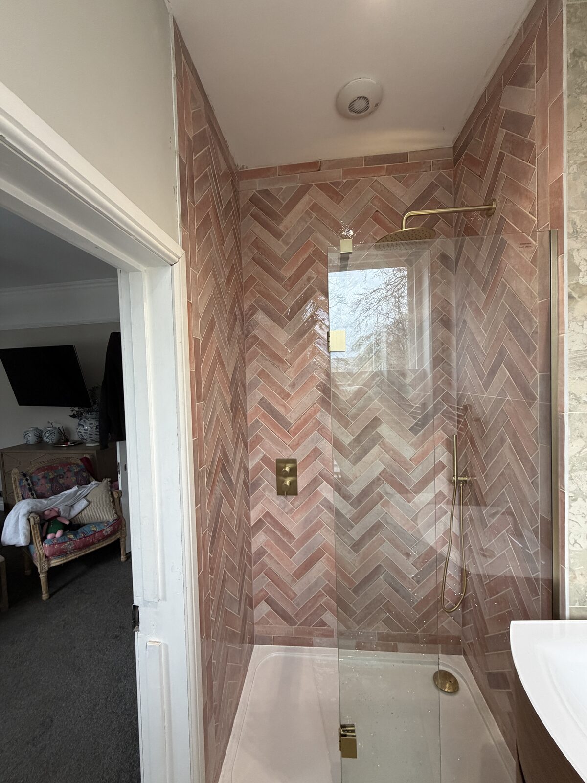 Herringbone-pattern terracotta brick tiling in a shower enclosure with brass fittings