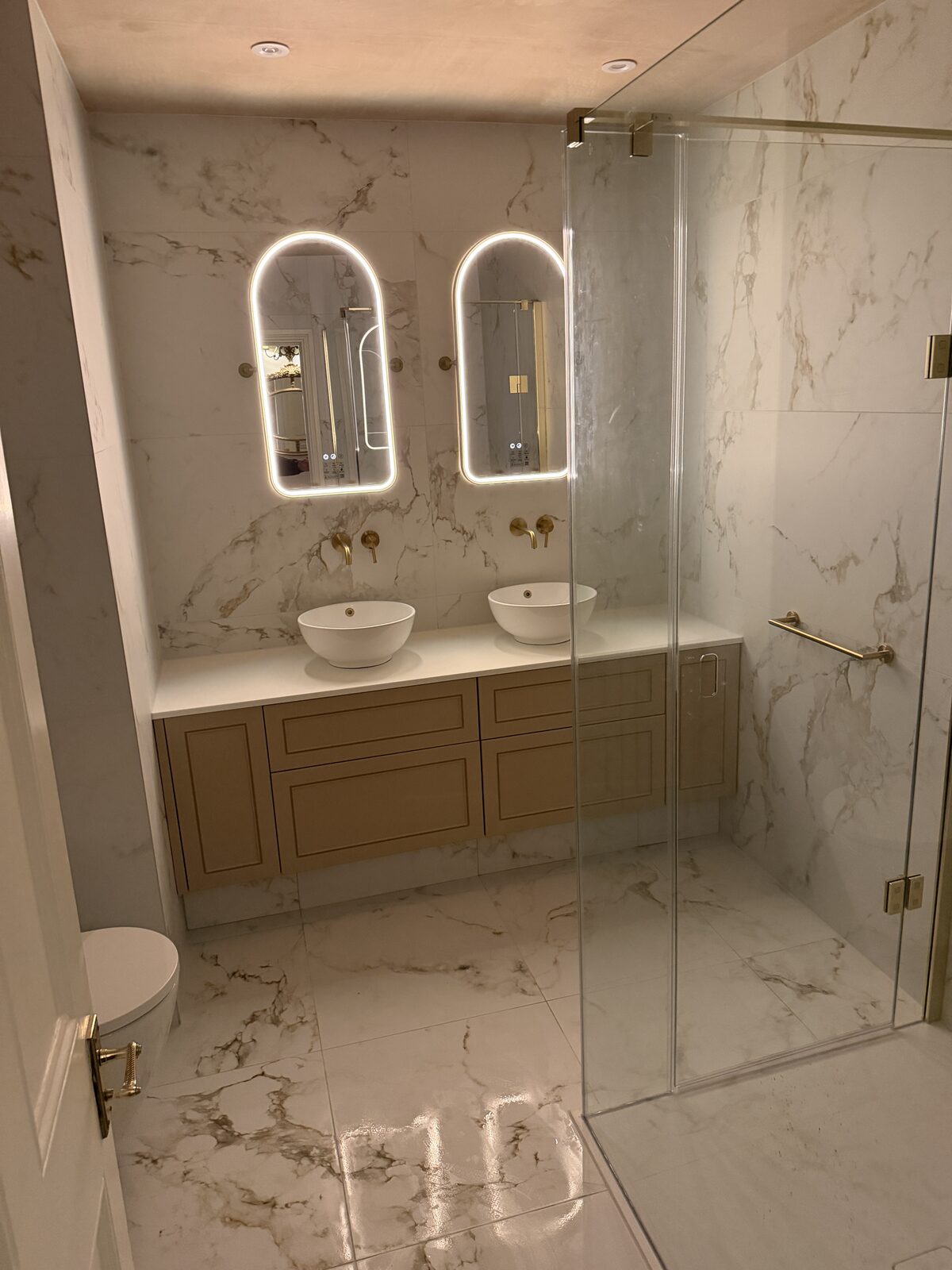 Full bathroom fit-out with double vanity, marble tiling and glass shower screen